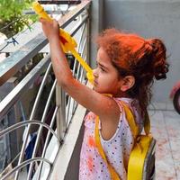 Sweet little Indian girl playing colours on Holi festival, holding pichakaree full of colours, Holi festival celebrations in Delhi, India photo