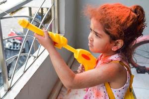 Sweet little Indian girl playing colours on Holi festival, holding pichakaree full of colours, Holi festival celebrations in Delhi, India photo