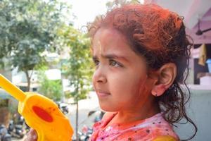 Sweet little Indian girl playing colours on Holi festival, holding pichakaree full of colours, Holi festival celebrations in Delhi, India photo