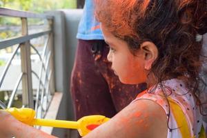 Sweet little Indian girl playing colours on Holi festival, holding pichakaree full of colours, Holi festival celebrations in Delhi, India photo