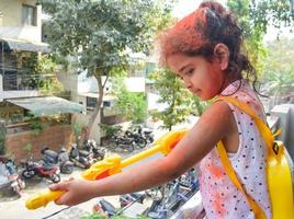 Sweet little Indian girl playing colours on Holi festival, holding pichakaree full of colours, Holi festival celebrations in Delhi, India photo