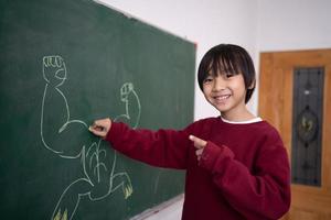 Happy school  Portrait of little boy writing on greenSchool, chalk and boy drawing on a board for child development, creativity and art for learning. Academic, creative and young kid student. photo