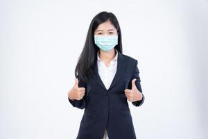 A confident beautiful young Asian business woman wearing green medical face mask and black suit, standing with her arms folded and looking at camera isolated on white background. photo