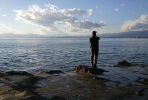 paisaje espectacular en la costa de enoshima, japón, con un pescador solitario parado al borde del agua foto