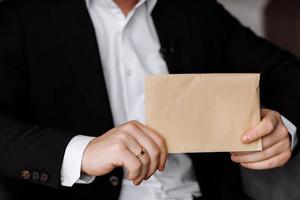 the groom holds an envelope with a letter from the bride. man is reading and sitting in the chair near the window. A letter for the groom. declaration of love. photo