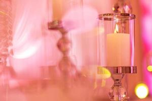 festive wedding table with burning candles and crystal in pink light. Crystal candle holder as a center piece at a wedding reception. photo