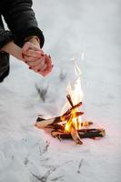 cropped photo of young woman warms her hands over bonfire in winter forest. Close-up