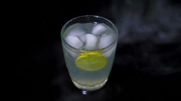 lemonade with ice in crystal glass with smoke on black background video