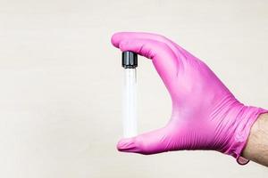 gloved hand holds closed test-tube over desk photo