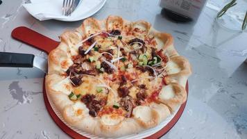 classic pizza with cheese on the table in a cafe on a wooden stand with a cut triangular piece and a pizza knife photo