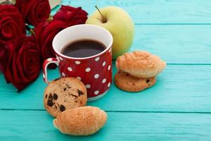 Cup of coffee with croissants and cookies and red roses on blue wooden background. Copy space. Mock up. Top view. Valentine mother day. photo