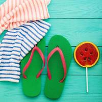 Summer accessories. Flip flops, sunglasses, towel, red cap and oranges on blue wooden background. copy space. photo