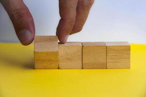 Hand turning wooden cube on yellow background. Customizable space on wooden cubes for text. Copy space concept. photo