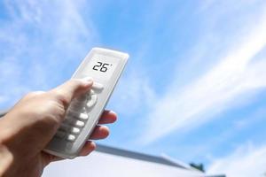 Close up of hand holding remote air conditioner on sky background. Concept of temperature control for global warming. photo