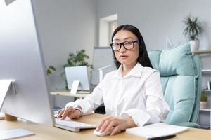 en línea distancia aprendiendo. joven asiático hembra profesor en auriculares sentado a un computadora enseñando foto