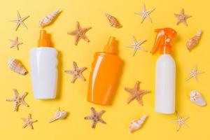 sunscreen cream with starfish and seashells in bottles on yellow background, top view photo