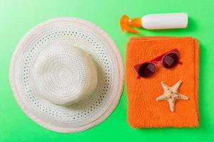 Summer beach flat lay accessories. Sunscreen bottle cream, towel and seashells on colored Background. Travel holiday concept with copy space photo