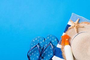 Summer beach flat lay accessories. Sunscreen bottle cream, straw hat, flip flops, towel and seashells on colored Background. Travel holiday concept with copy space photo
