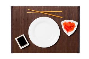 Empty round white plate with chopsticks for sushi, ginger and soy sauce on dark bamboo mat background. Top view with copy space for you design photo