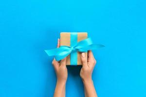 Woman arms holding gift box with blue ribbon on color background, top view photo