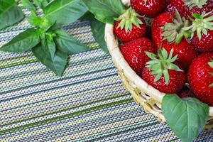 fresas dulces maduras en cesta de mimbre y hojas de menta. foto