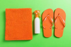 Top view of Beach flat lay accessories. sunscreen bottle with seashells, starfish, towel and flip-flop on Colored background with copy space photo
