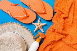 Summer beach flat lay accessories. Sunscreen bottle cream, straw hat, flip flops, towel and seashells on colored Background. Travel holiday concept with copy space photo
