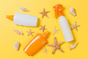 Sunscreen bottles with seashells on yellow table top view photo