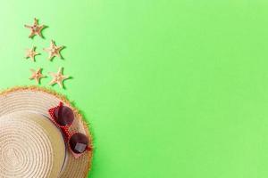 Summer holiday background with straw hat and seashells on green background top view with copy space photo