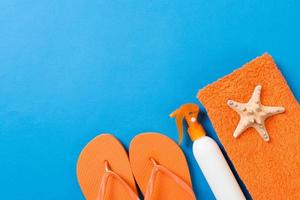 Top view of Beach flat lay accessories. sunscreen bottle with seashells, starfish, towel and flip-flop on Colored background with copy space photo