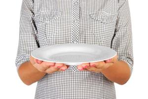 la chica de la camisa a cuadros sostiene un plato blanco redondo vacío frente a ella. mano de mujer sostenga el plato vacío para su diseño. vista en perspectiva, aislada sobre fondo blanco foto