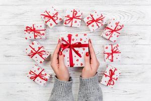 Woman hands give wrapped valentine or other holiday handmade present in paper with red ribbon. Present box, red heart decoration of gift on wooden table, top view with copy space for you design photo