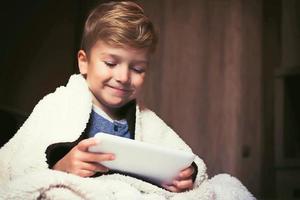 Cute boy using touchpad while being covered with blanket. photo