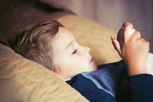 Little boy using touchpad while lying down on bed. photo