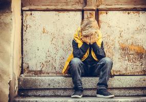 Sad boy with head in hands sitting on staircase outdoors. photo