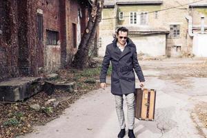 Smiling wan with suitcase walking among old buildings. photo