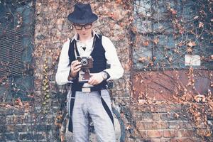 Retro styled man with vintage photo camera against brick wall.