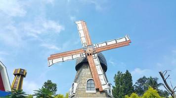 Windmill farmhouse with slowly rotating blades or propellers. A clear blue sky in background. photo