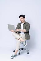 joven asiático negocio hombre sentado en silla y utilizando ordenador portátil en antecedentes foto
