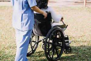 asiático joven cuidador enfermero apoyo mayor más viejo masculino caminando al aire libre. especialista niña médico ayuda y tomar cuidado de mayor maduro hombre paciente haciendo físico terapia en público parque a enfermería hogar. foto