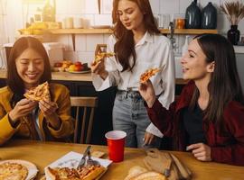 Young woman eating pizza and laughing while sitting with her friends in a restaurant. Group of friends enjoying while having food and drinks at cafe. photo