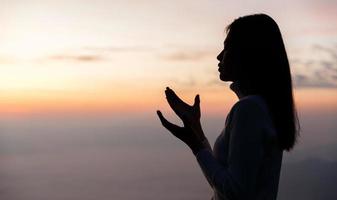 silueta de mujer Orando para gracias Dios Orando con su manos juntos a pensar de un amoroso dios, nosotros alabanza Dios con ligero llamarada en el verde naturaleza. foto