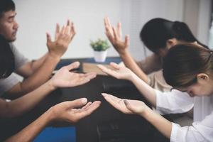 grupo de religioso personas Orando juntos adentro. grupo de personas participación manos y Orando mientras sentado en oficina. foto