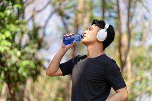 Male runner drinking water after running at green park photo