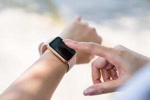 cerca arriba Disparo de femenino mano conmovedor un reloj inteligente a al aire libre en puesta de sol. foto