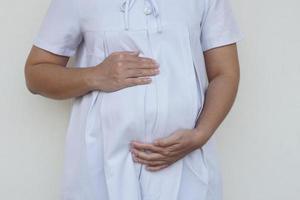 Closeup 6 month pragnant woman wears white dress, hands touch her big belly. Concept, pragnancy, motherhood. Health care. photo