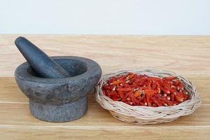 Old granite stone mortar with pestle and basket of red dried chillies for cooking. photo
