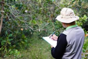 Asian man botanist is at forest to survey botanical plants, holds paper clipboard. Concept , Survey ,research botanical plants. Forest and environment conservation. photo