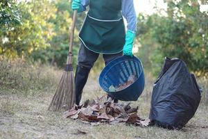 Closeup gardener holds broom , basket, black garbage bag to clean dry leaves in garden.                             Concept, get rid of dry leaves to make compost or make fire barrier in autumn. photo