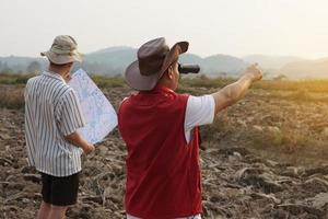 Asian father and son are exploring and surveying their own land, father holds binocular and points to boundary, son holds map. Concept, land property, legacy.Exploration. photo